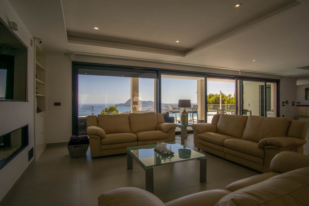 Spacious living area featuring leather seating, recessed ceiling lighting, and floor-to-ceiling glass doors with panoramic views of the Mediterranean coast.