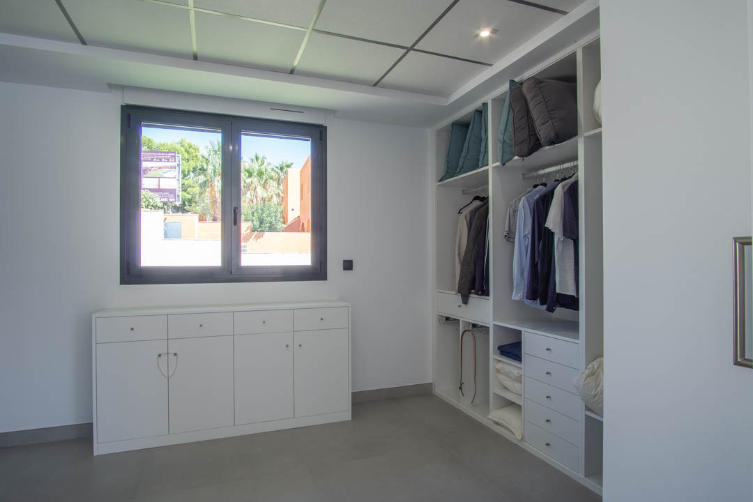 Walk-in closet featuring white open cabinetry, a low sideboard under a dark-framed window, and a grid ceiling with recessed lighting.