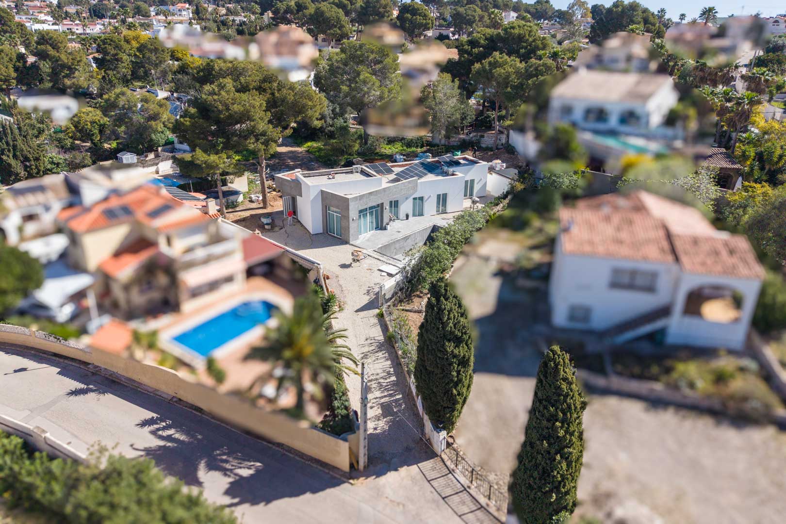 Aerial view of the minimalist villa featuring solar panels on the flat roof, highlighting the plot currently under development within a mature residential neighborhood.