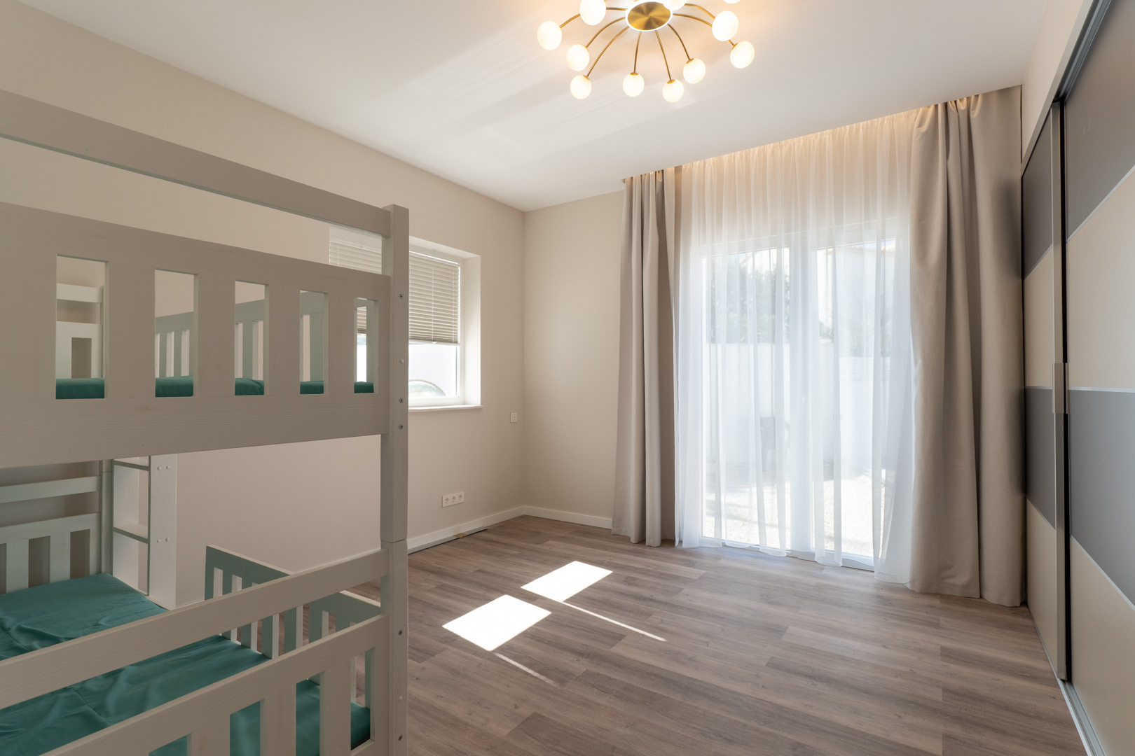 Bedroom featuring white wooden bunk beds, wood-effect flooring, and a large built-in wardrobe. Natural light fills the space through floor-to-ceiling windows.
