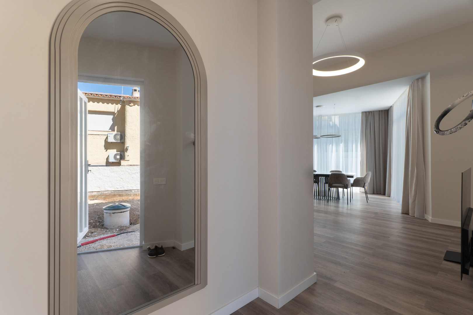 Entrance featuring an arched mirror reflecting the exterior, leading into a minimalist living area with wood-effect flooring and a modern circular pendant.