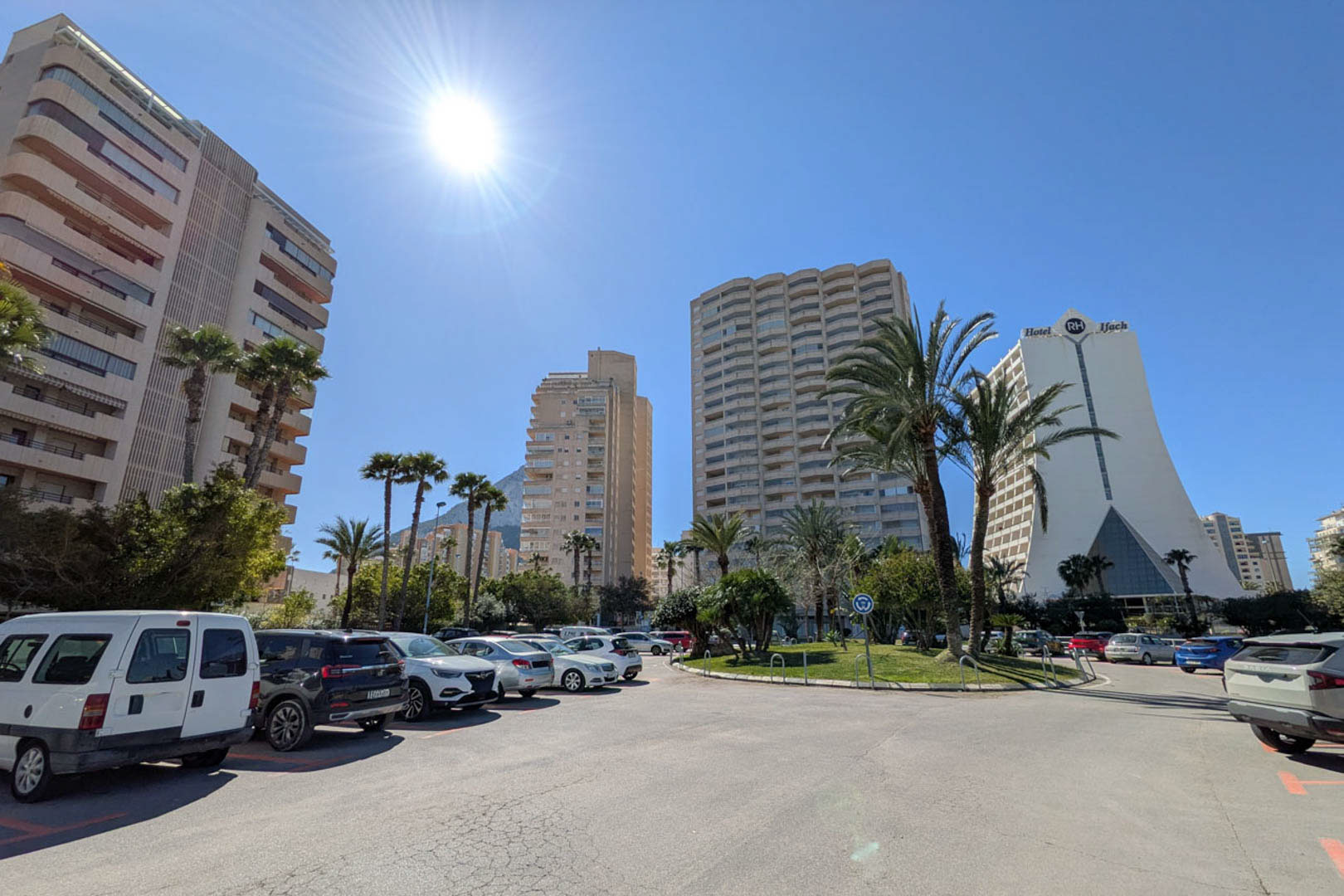 Exterior view of an urban district in Calpe, featuring high-rise residential complexes, the RH Ifach Hotel, and public parking under a clear sky.