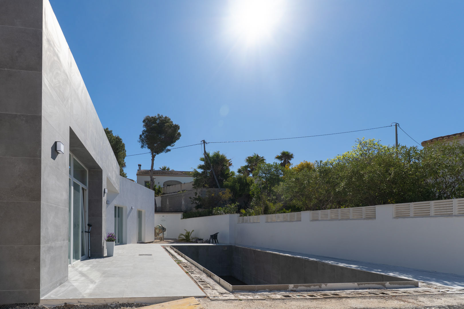 Minimalist facade featuring grey stone cladding and a swimming pool currently under construction, set against a clear sky and white perimeter walls.