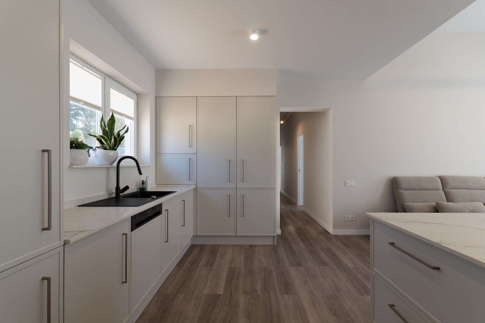 Minimalist kitchen featuring matte white cabinetry, veined stone countertops, and a black faucet. The functional layout includes wood-effect flooring and natural light.