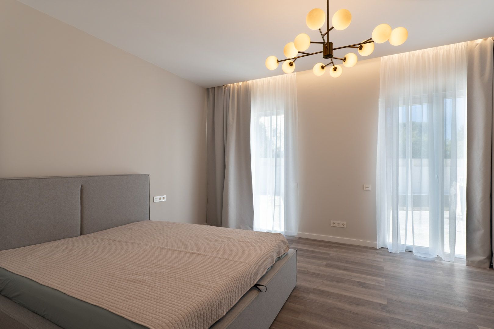 Minimalist master bedroom featuring grey wood flooring, indirect LED cove lighting, and a contemporary molecular globe chandelier.