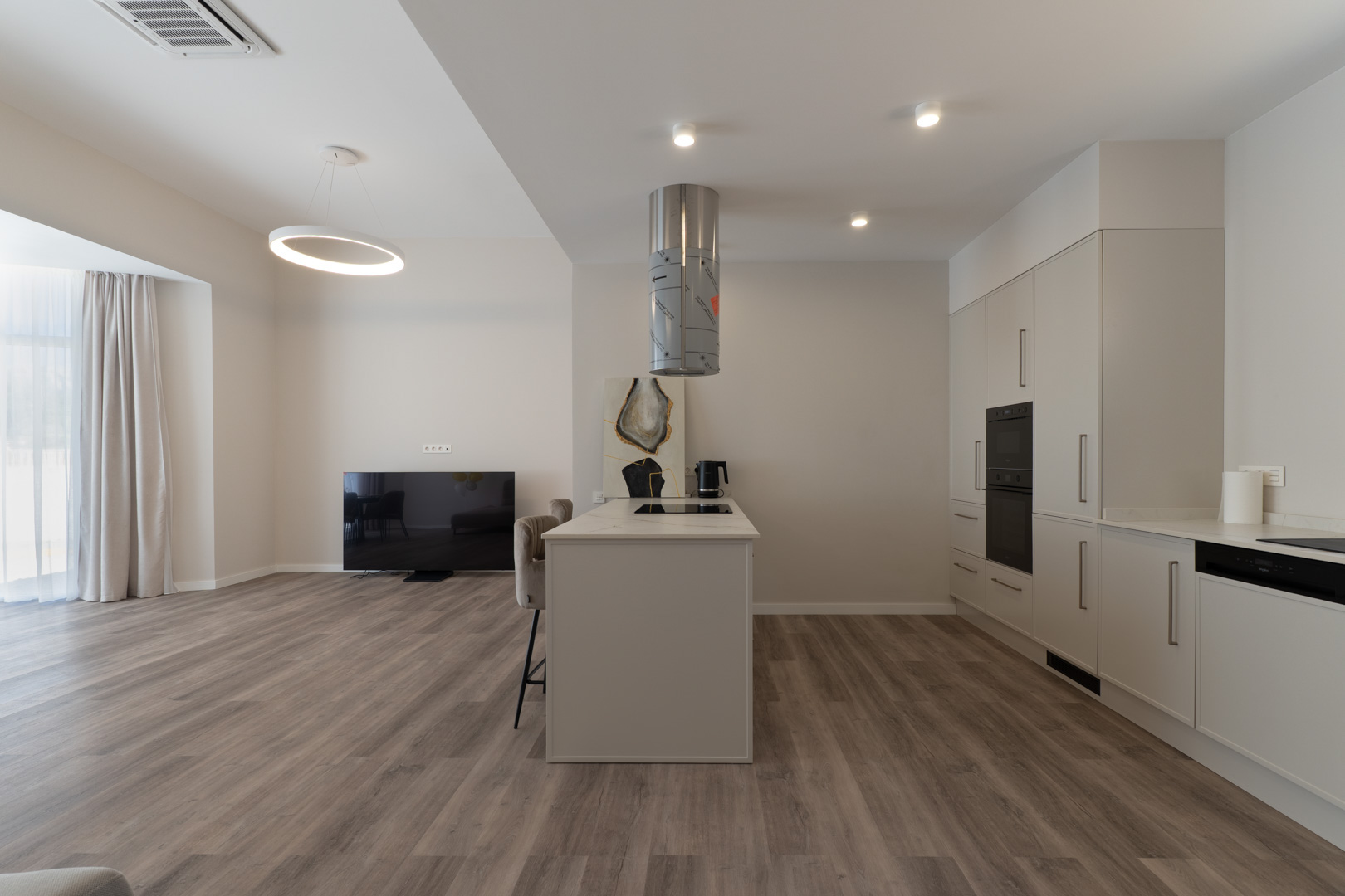 Open-concept kitchen featuring a central island with marble-effect countertop, cylindrical extractor, and integrated appliances set against wood-effect flooring.