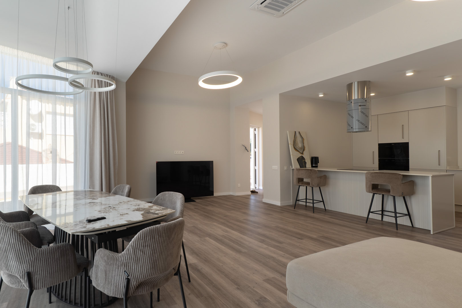 Open-concept living space featuring a marble dining table, minimalist kitchen with breakfast bar, and contemporary circular LED pendant lighting.
