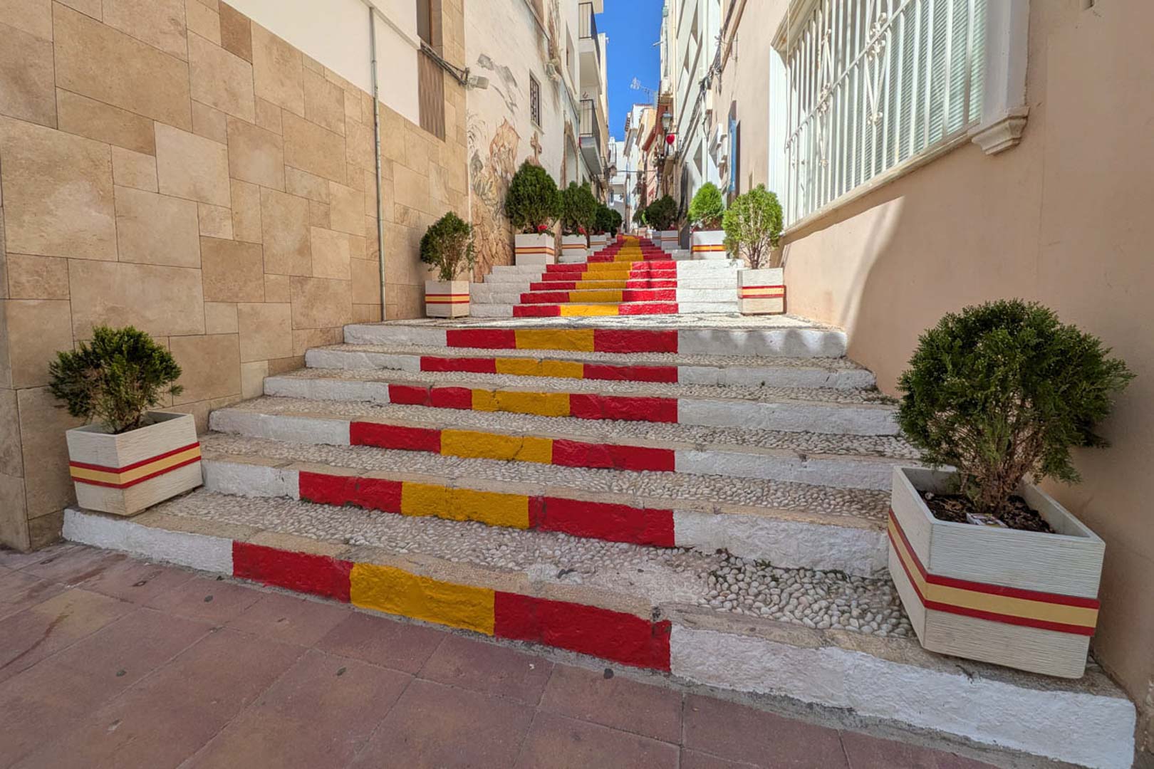 Pedestrian street in Calpe's old town featuring a stone staircase painted with the Spanish flag colors, accented by ornamental planters and traditional architecture.