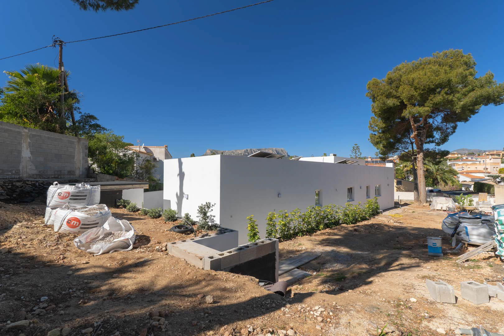 Single-story minimalist villa with a clean white facade and rooftop solar panels. The exterior grounds are currently in the landscaping and leveling phase.