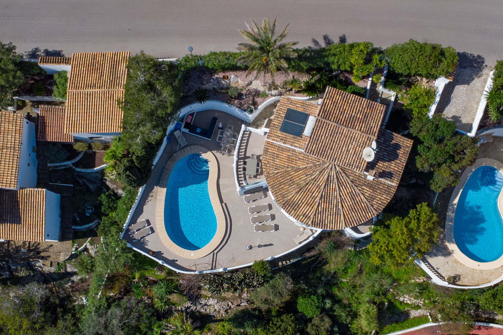 Aerial perspective showing the kidney-shaped pool, expansive sun terrace with outdoor dining, and traditional roof architecture with solar panels.