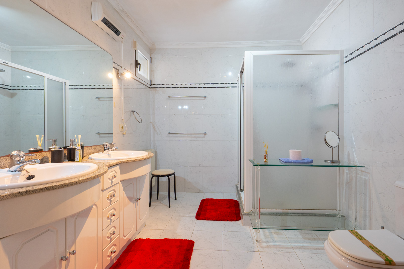Bathroom featuring a double vanity with granite countertops and white cabinetry. It includes a walk-in shower with frosted glass and split air conditioning.