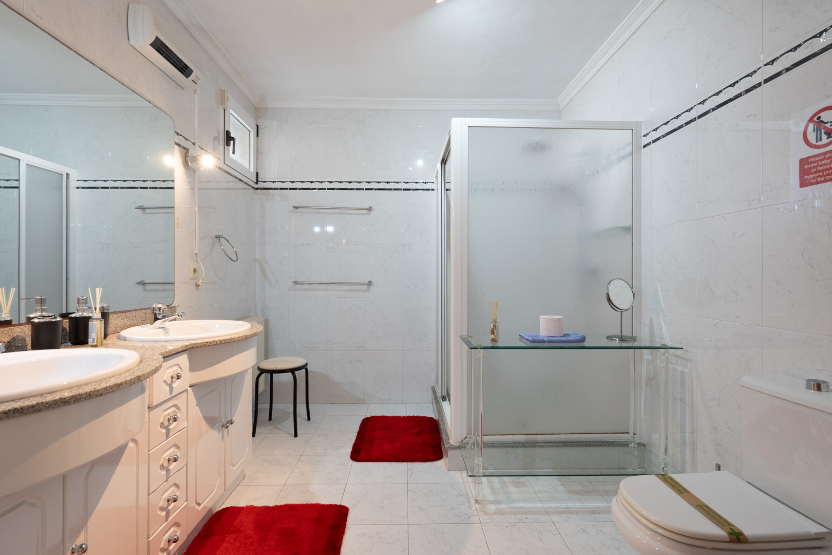 Bathroom with a double vanity, granite countertop, large mirror, and a walk-in shower with frosted glass. Includes split air conditioning and tiled walls.