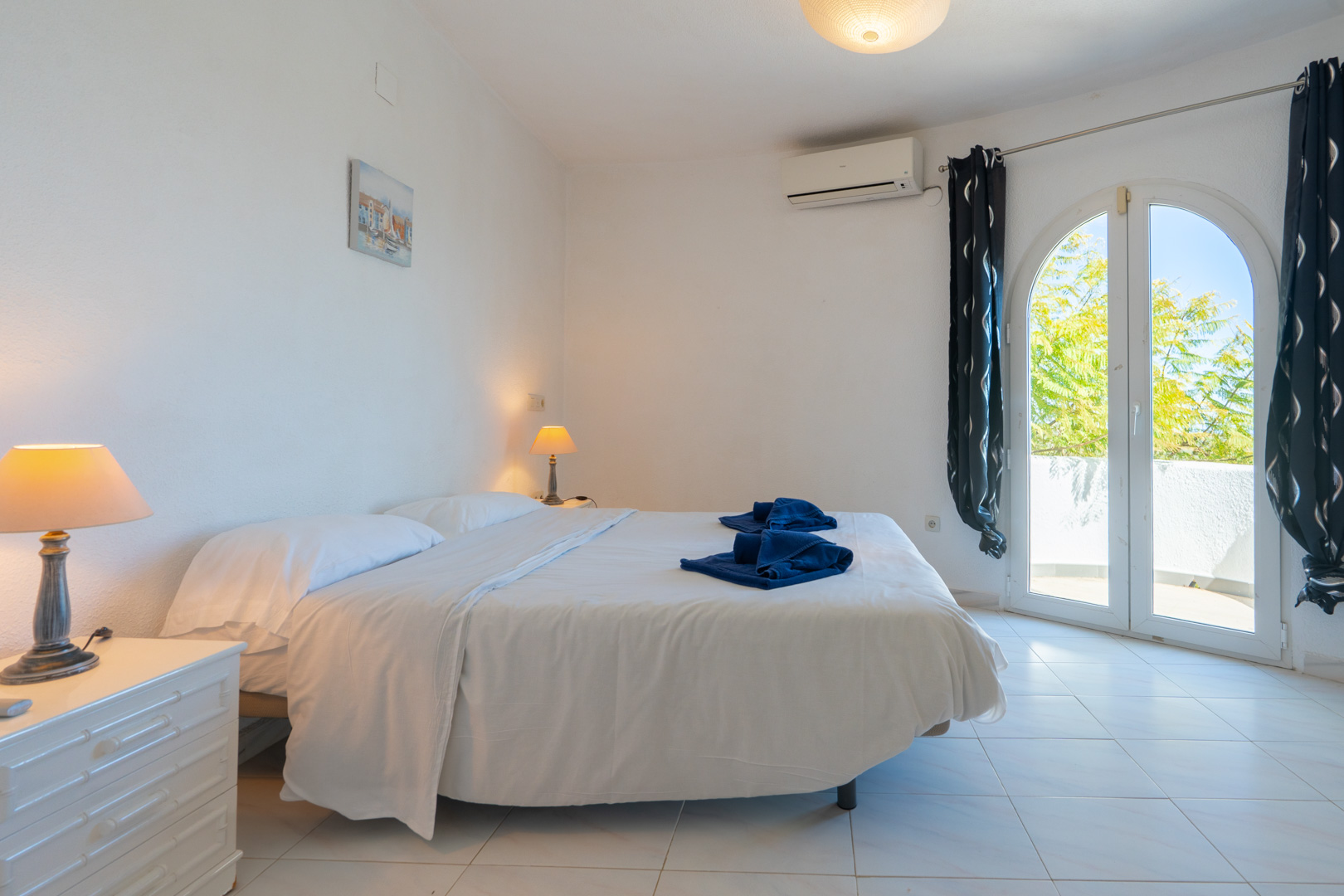 Bright bedroom featuring a double bed, split-system air conditioning, and an arched glass door opening onto a private terrace.