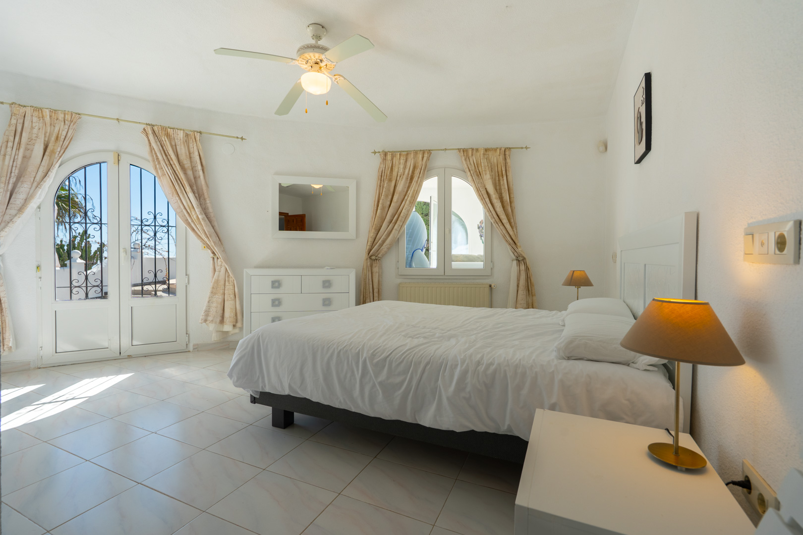 Bright bedroom featuring tiled flooring, a ceiling fan, and direct outdoor access through an arched glass door with decorative security ironwork.