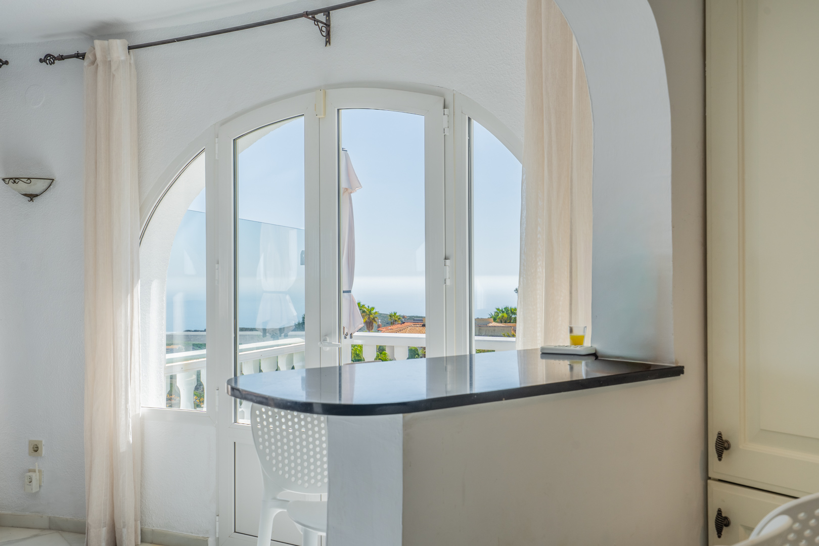 Dark stone breakfast bar set within a white archway, featuring views of the Mediterranean through large arched windows and terrace doors.