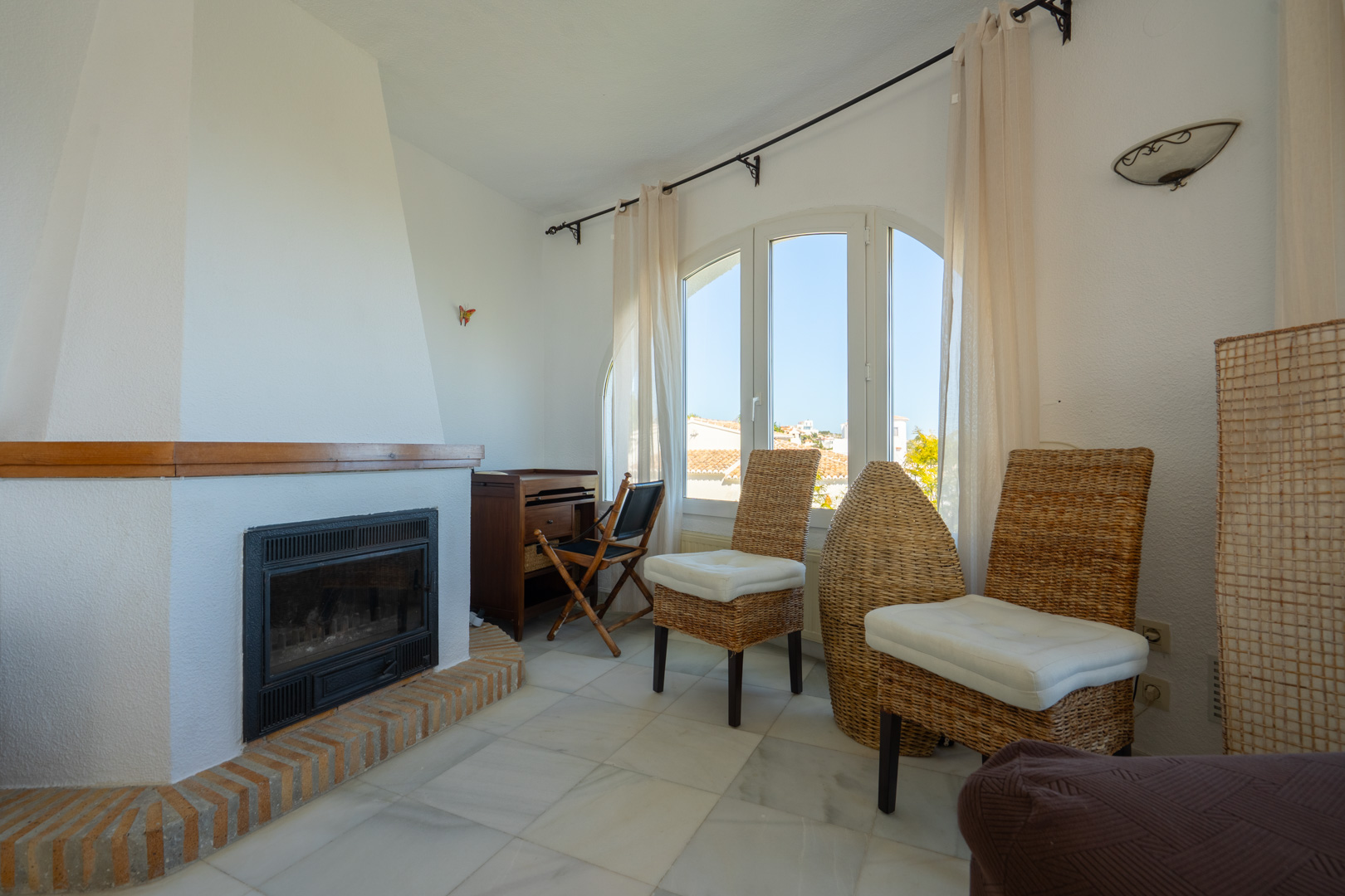 Living area featuring a built-in fireplace with a brick base, marble flooring, and an arched window providing natural light to the traditional seating space.
