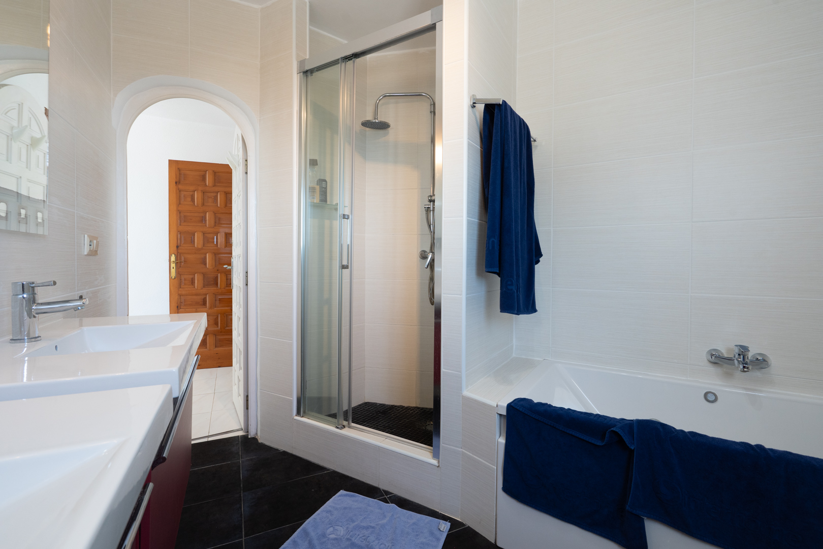 Modern bathroom featuring a double vanity, a built-in bathtub, and a separate walk-in shower with a glass enclosure, chrome fixtures, and textured wall tiles.