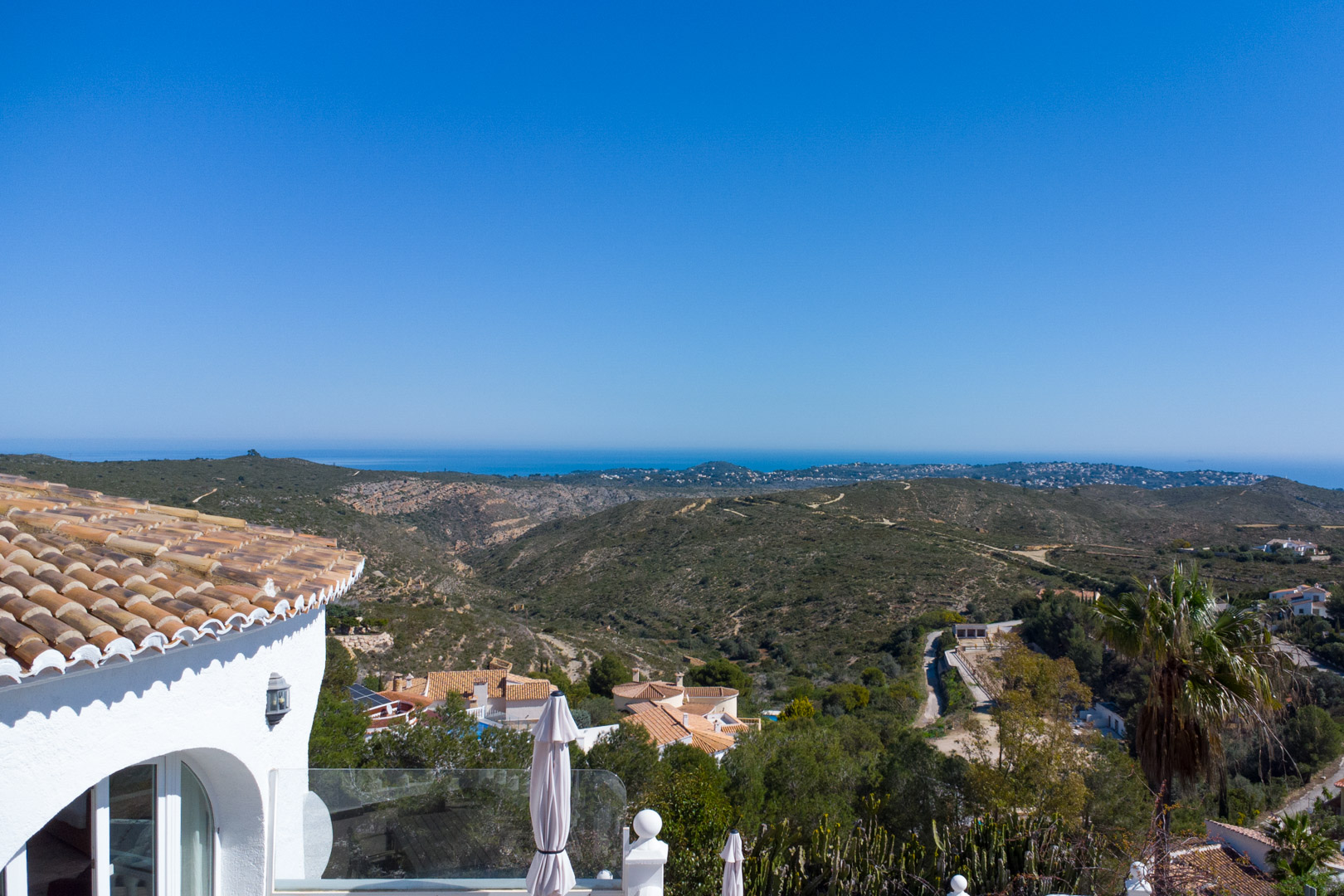 Panoramic views from the villa overlooking the Granadella natural park and the Mediterranean Sea, featuring traditional terracotta roofing and white curved walls.