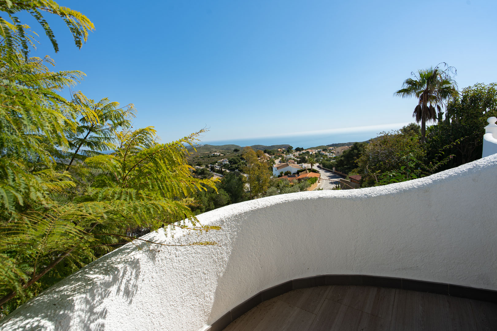 Terrace featuring a curved white textured wall and dark floor tiles, overlooking the Mediterranean Sea and the lush landscape of Cumbre del Sol.