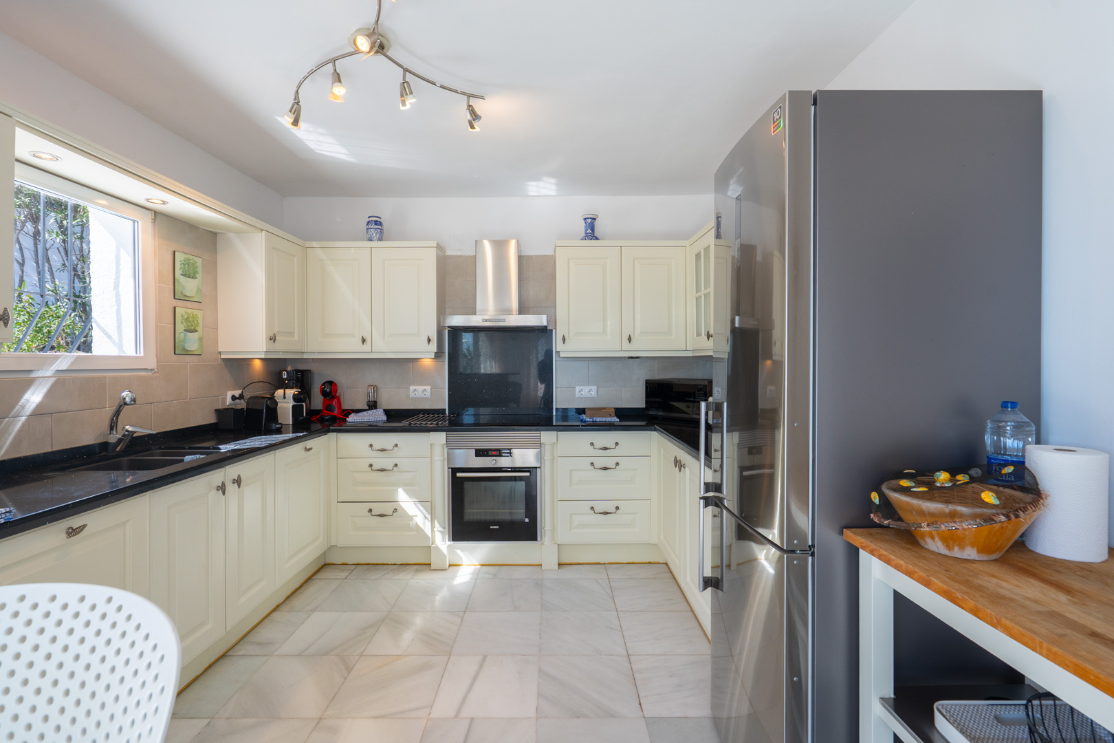Traditional U-shaped kitchen featuring cream cabinetry, black granite countertops, and stainless steel appliances set on light marble flooring.