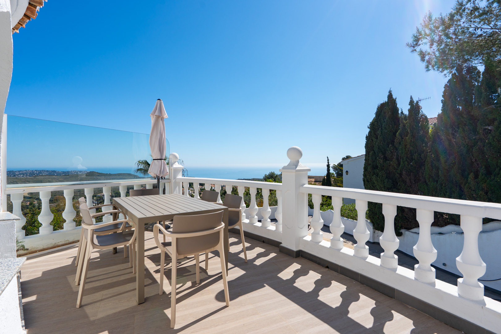Upper terrace featuring a white balustrade, modern dining furniture, and panoramic views of the Mediterranean Sea and surrounding nature park.