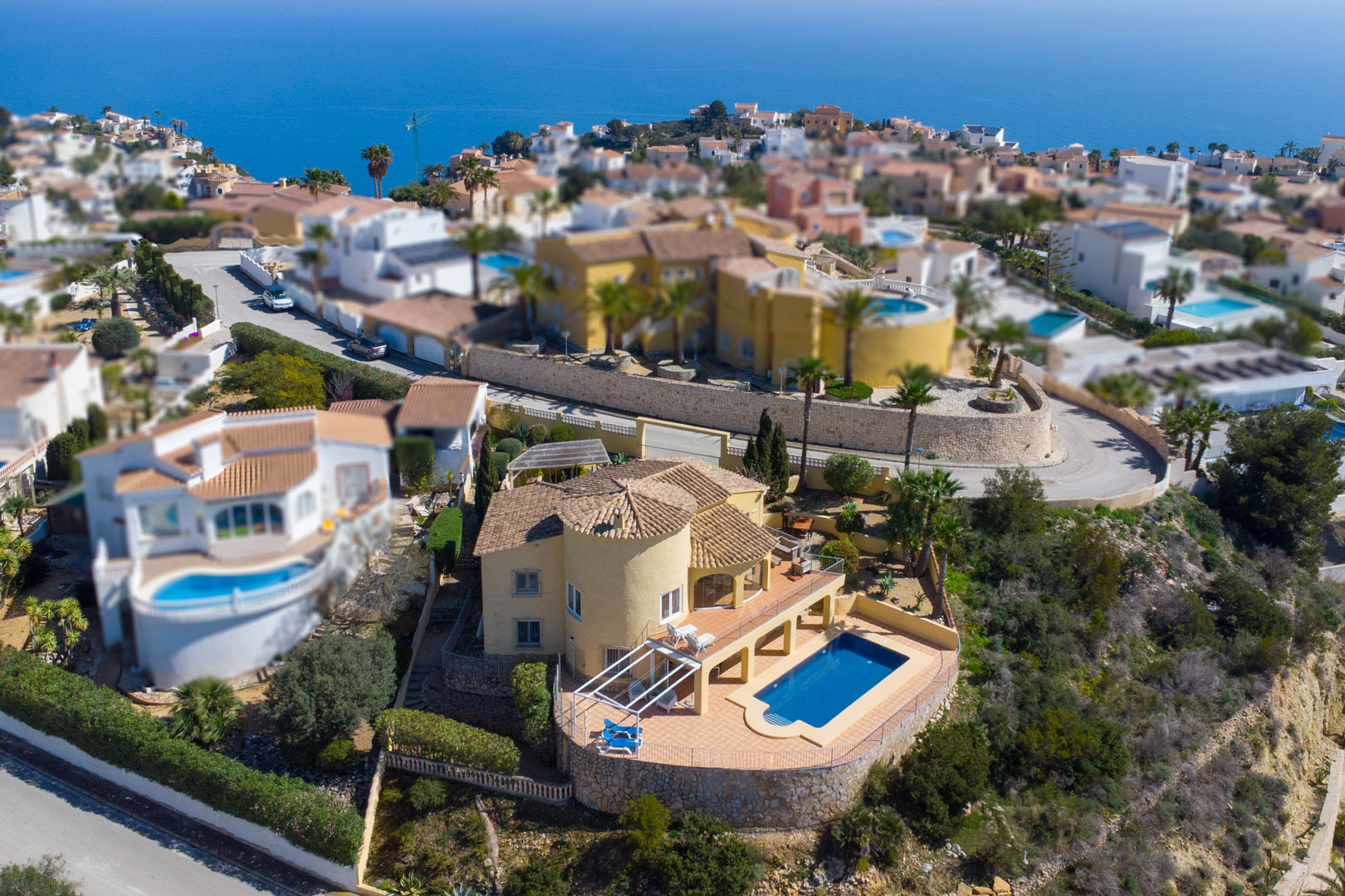 Aerial view of the traditional villa featuring a yellow facade, circular tower, and private pool area with a spacious sun terrace overlooking the Mediterranean.