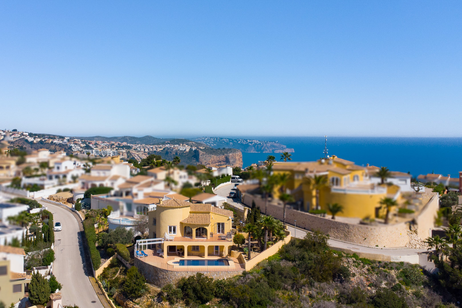 Aerial view of the yellow-facade villa featuring a private pool and multi-level terraces with panoramic views of the Mediterranean Sea and Cap d’Or.