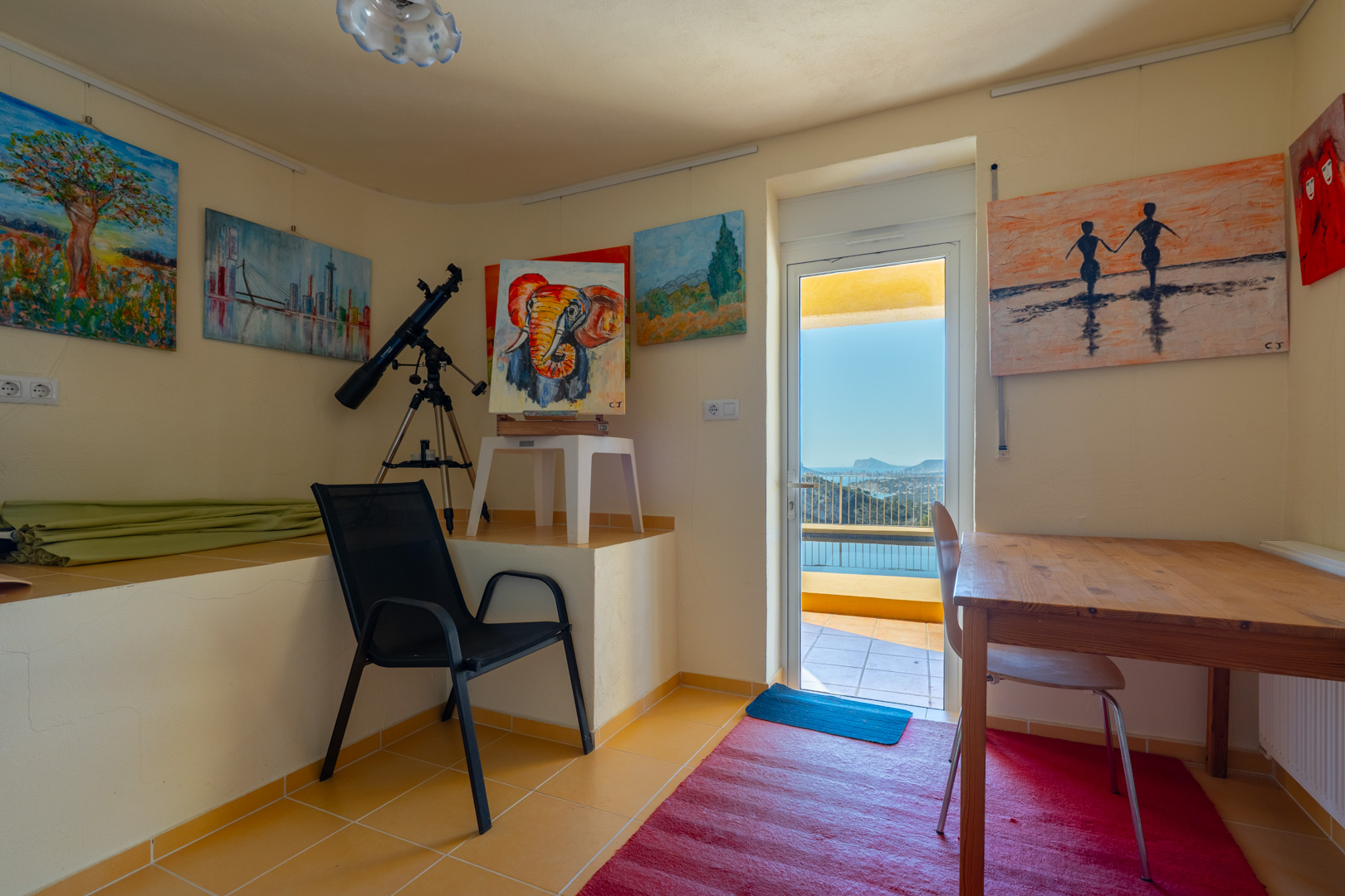 Bright home office and art studio featuring a telescope, wooden desk, and direct access to a terrace with panoramic Mediterranean views.
