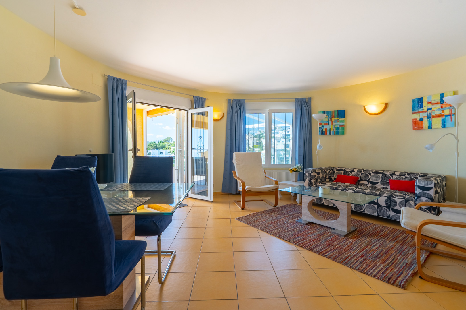 Bright open-plan living and dining area featuring ceramic tile flooring, modern furnishings, and direct access to the outdoor terrace through glass doors.