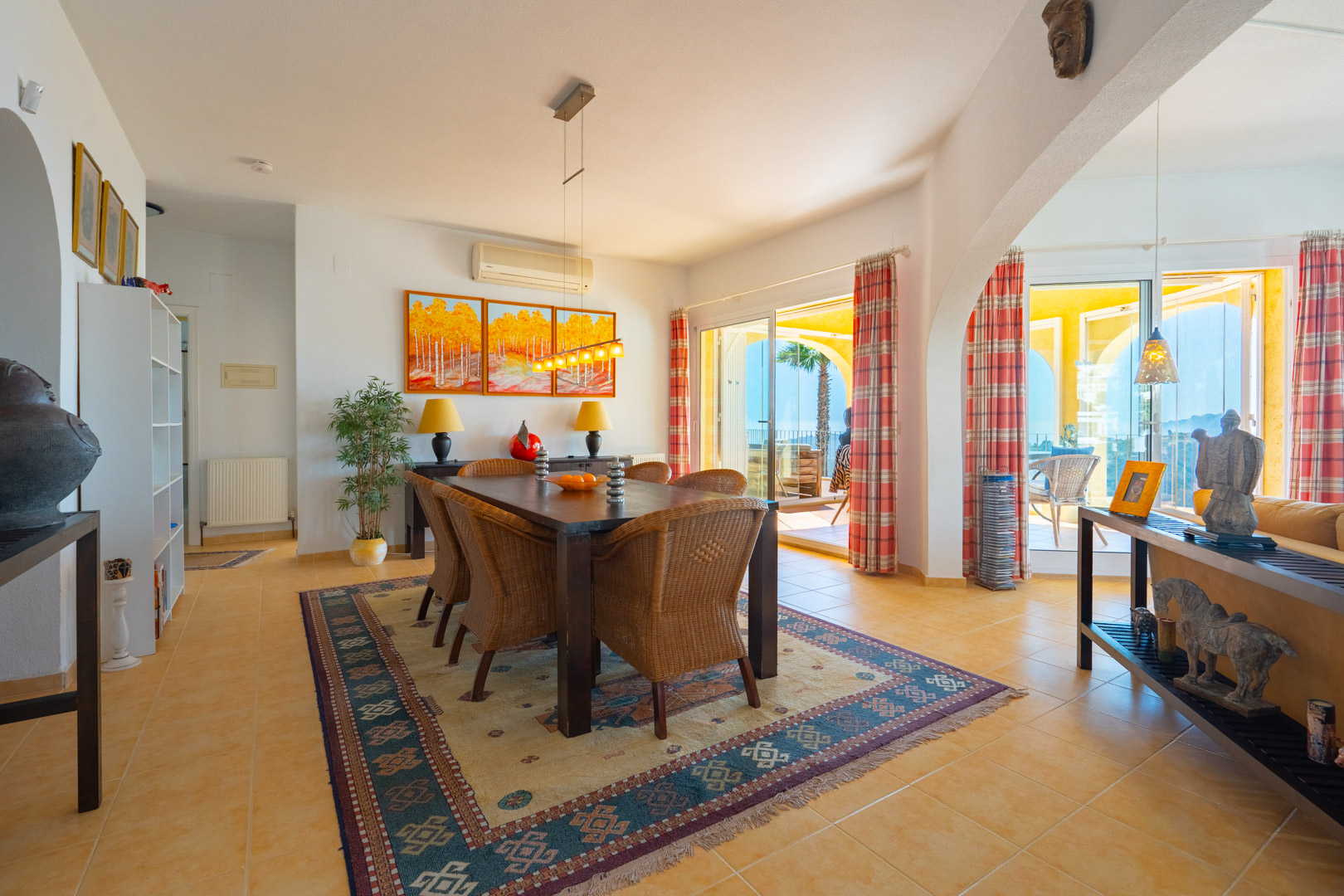 Dining area featuring a dark wood table with wicker chairs and terracotta tiling, offering direct access to the arched terrace and panoramic views.