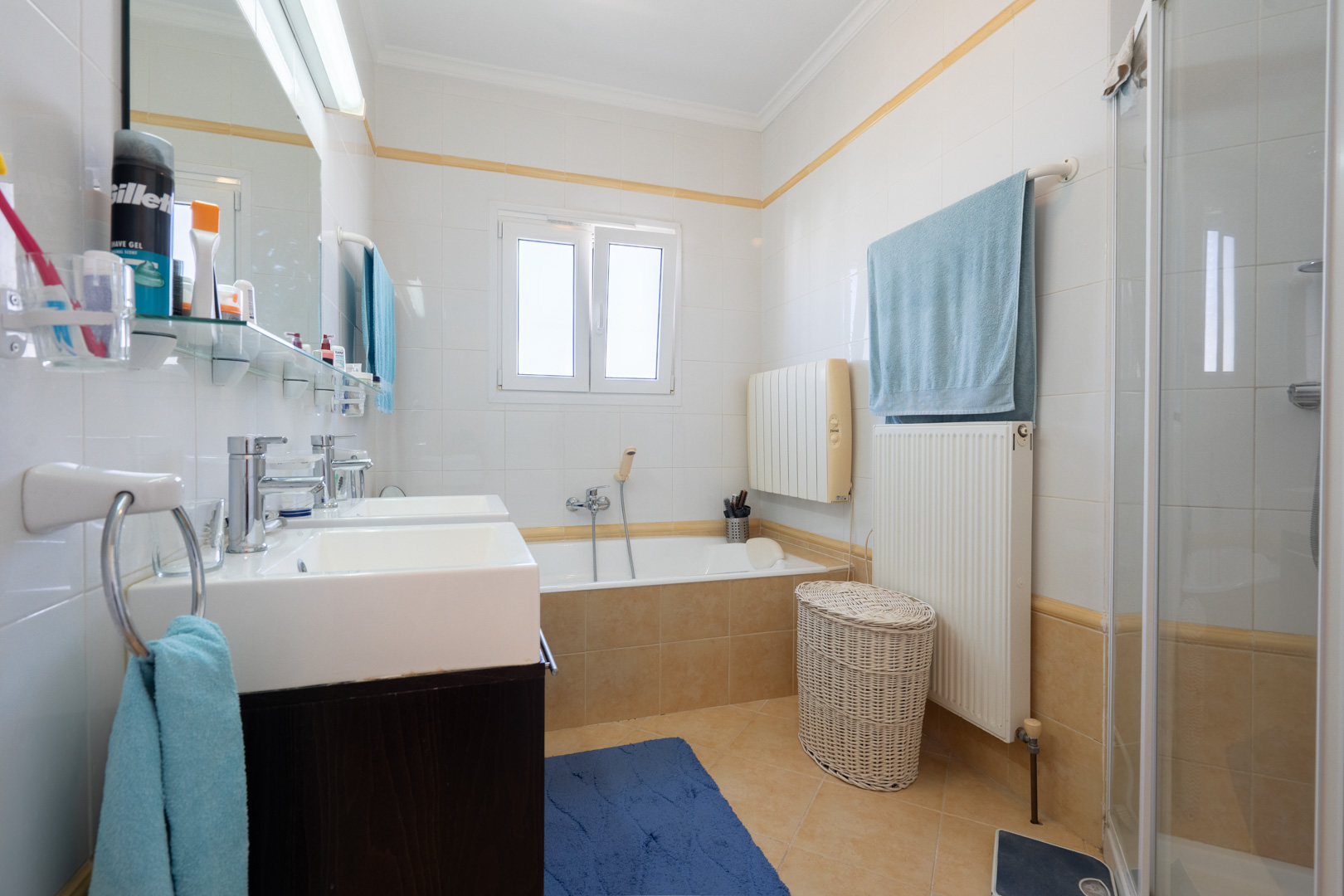 Full bathroom featuring a double vanity, built-in bathtub, separate shower enclosure, and white tiling with decorative yellow accents.