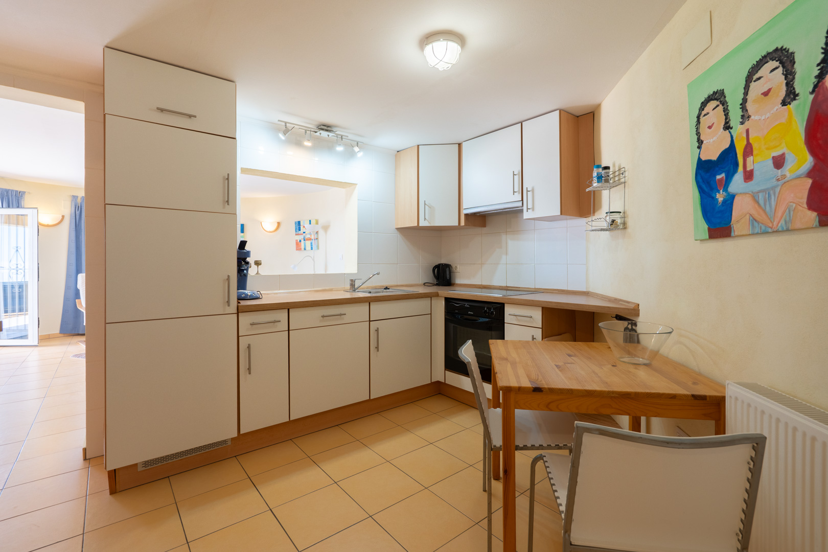 Functional kitchen featuring white cabinetry with wood trim, a wooden countertop, and an integrated dining area. Includes a pass-through window and tiled flooring.