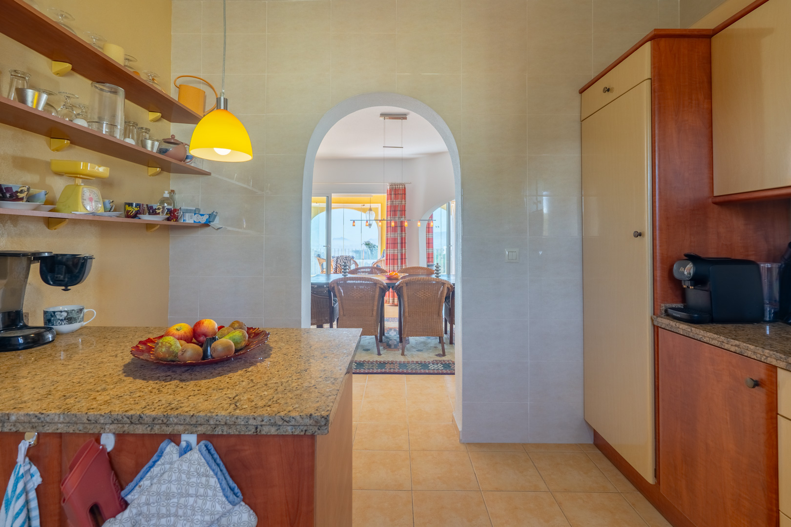 Functional kitchen with granite countertops and open shelving, connected through an arched doorway to the dining area and terrace.