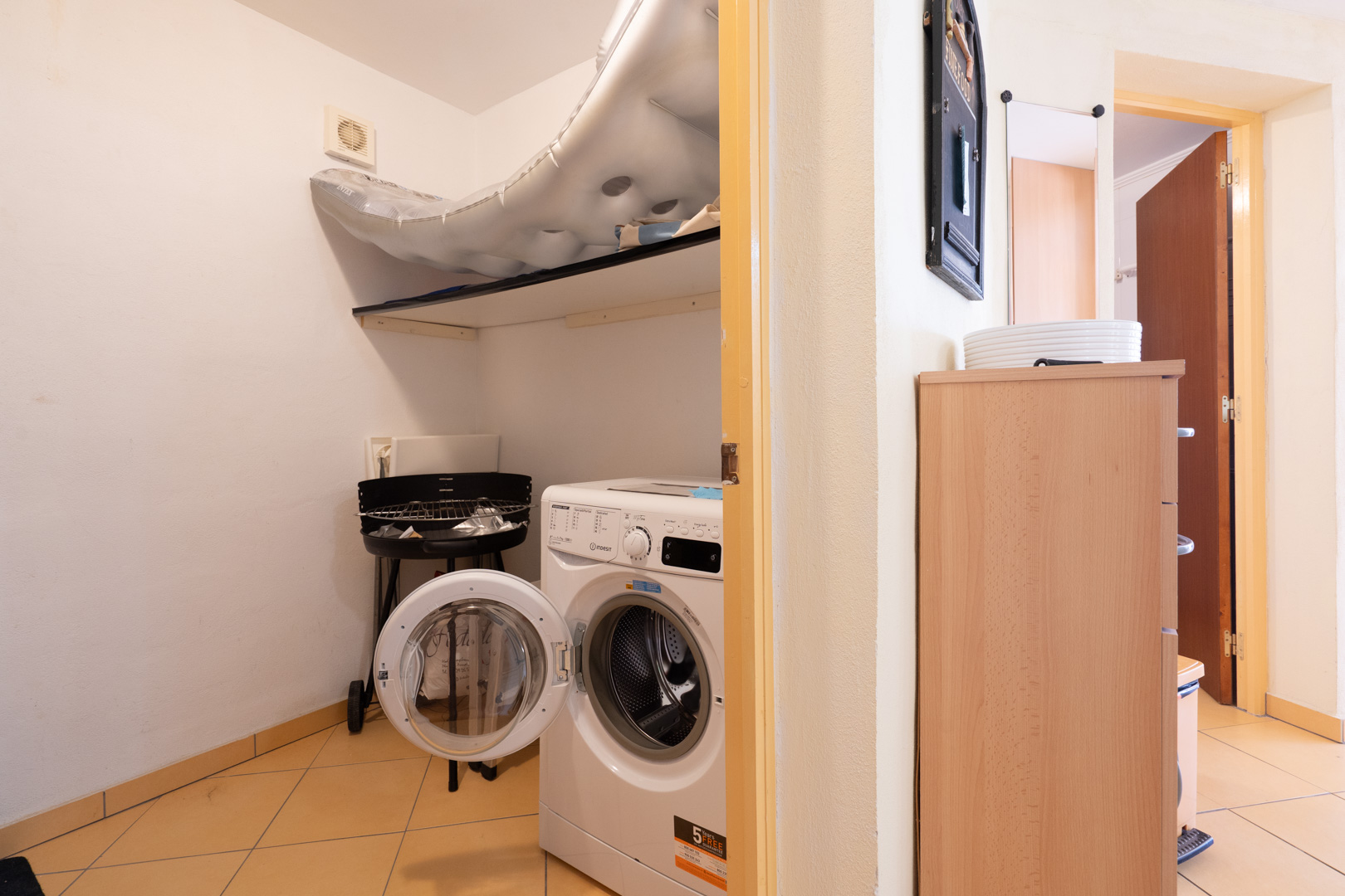 Functional laundry room featuring a front-loading washing machine, overhead storage shelving, and neutral tiled flooring.
