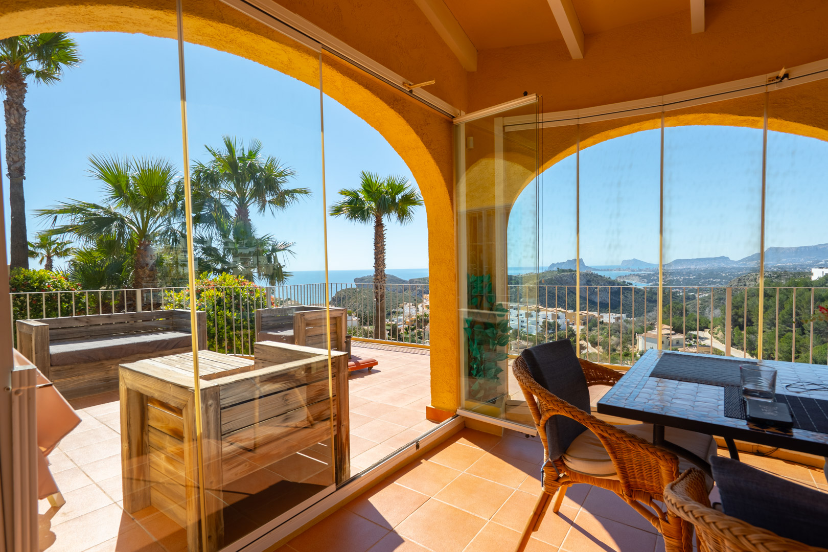 Glass-enclosed naya with terracotta tiles and exposed beams, featuring panoramic views of the Mediterranean coastline and the Peñón de Ifach.