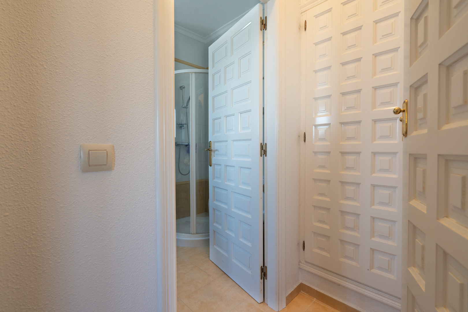 Hallway featuring white paneled built-in wardrobes and an open door leading to a bathroom with a curved corner shower unit.