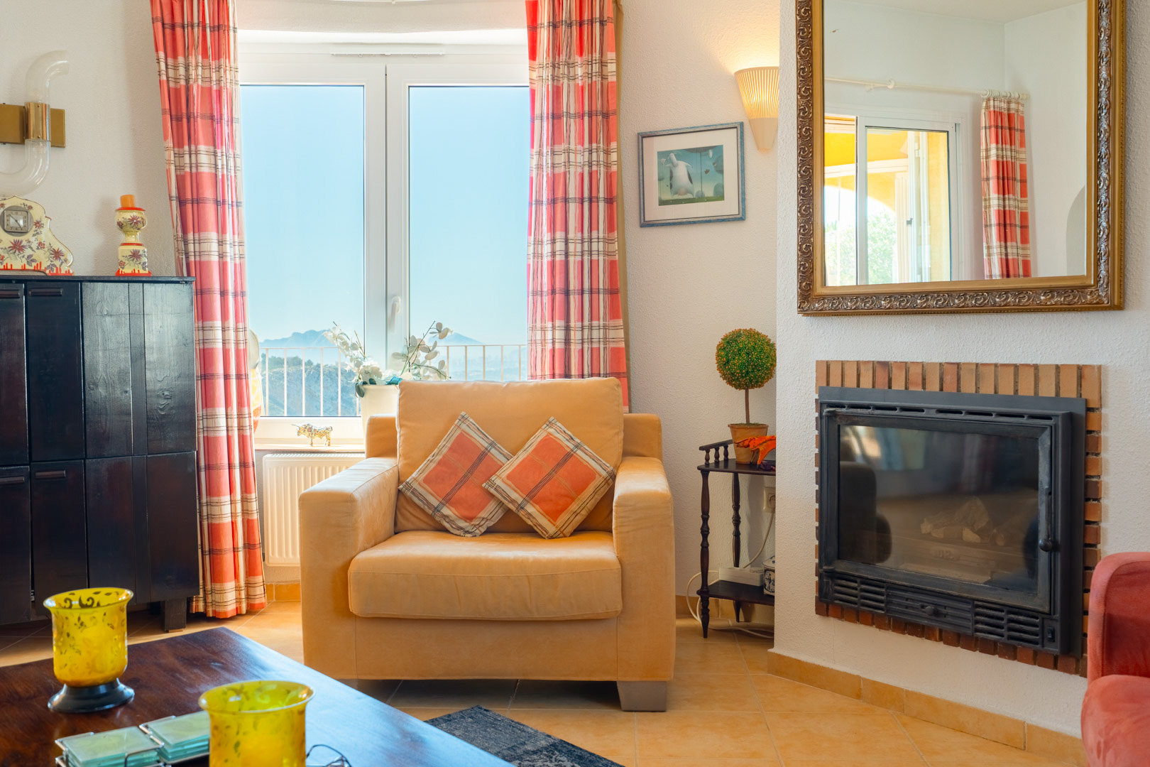 Living area featuring a built-in fireplace with brick detailing, a comfortable armchair, and a window offering views of the inland mountains.