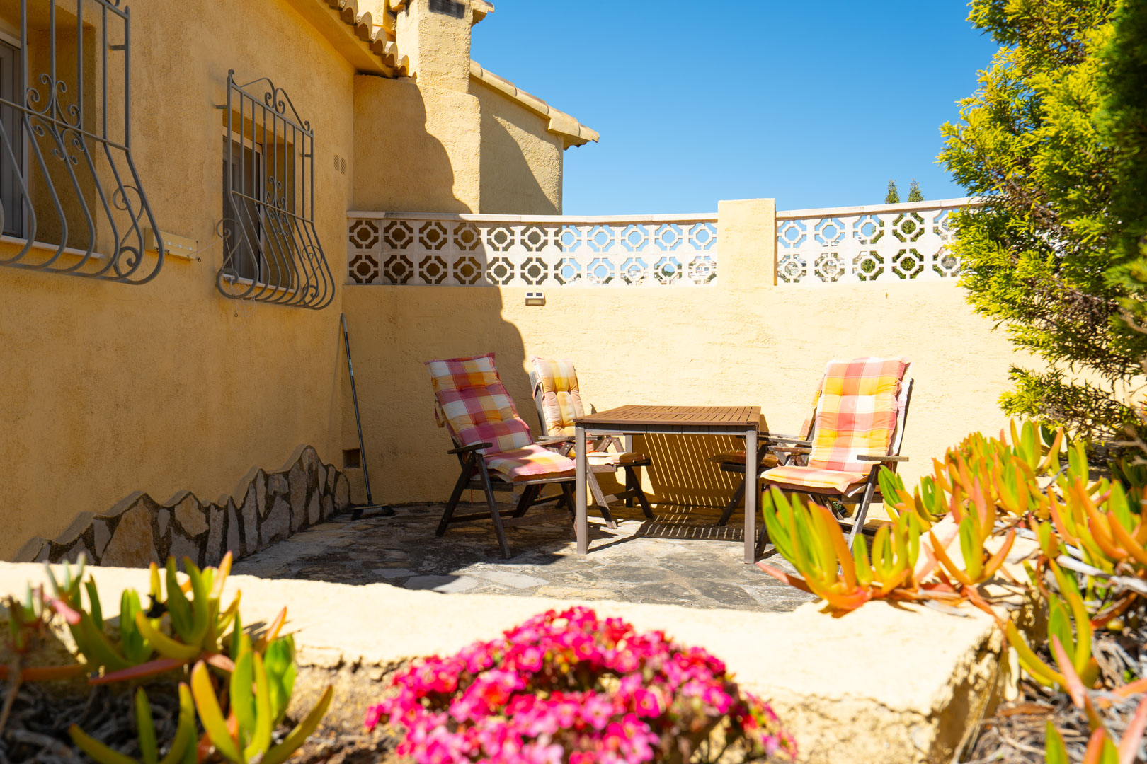Outdoor terrace featuring natural stone flooring, wooden dining furniture, and traditional wrought iron window grilles against an ochre facade.