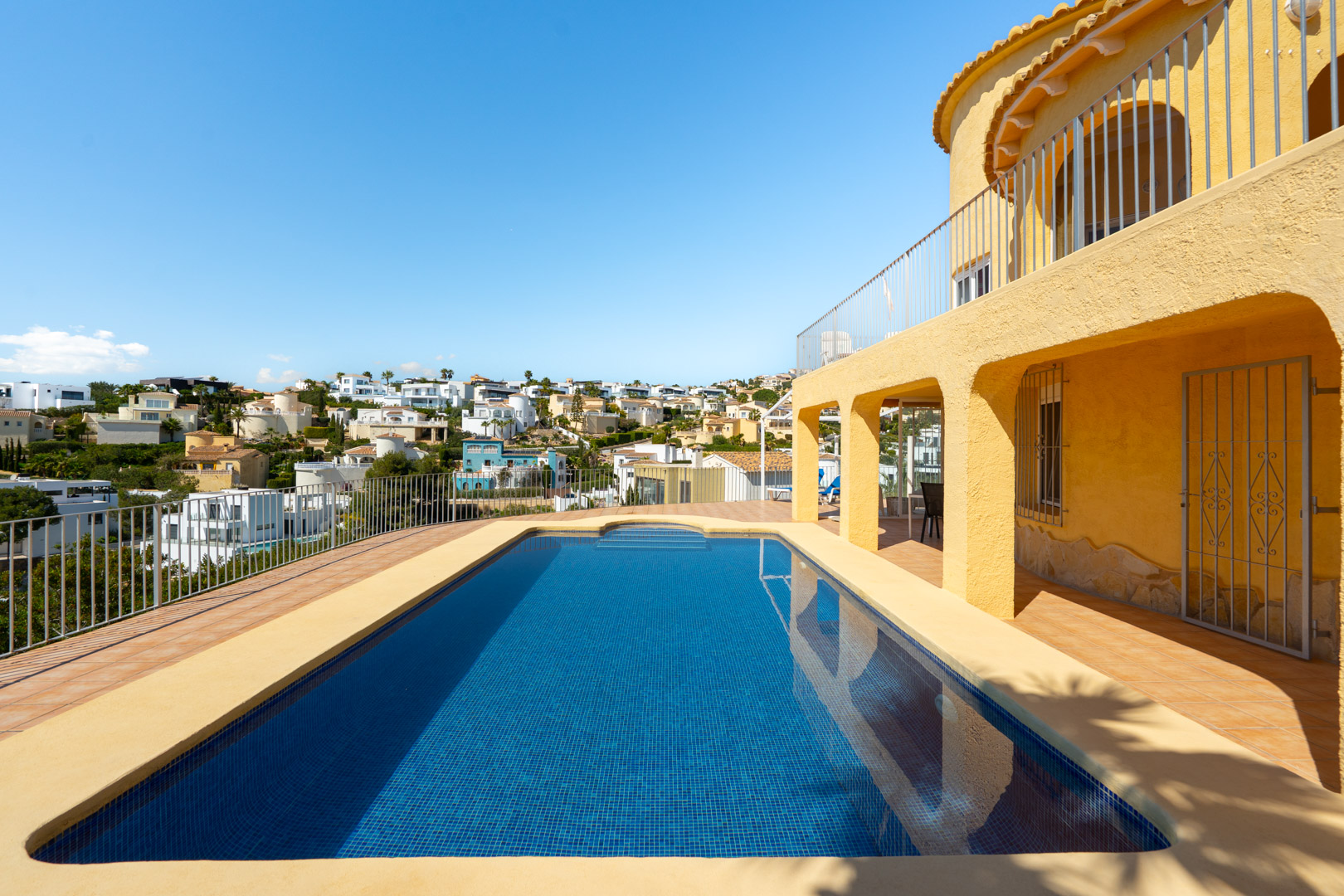 Rectangular swimming pool with blue mosaic tiles, featuring a spacious sun terrace and arched porch overlooking the surrounding residential landscape.