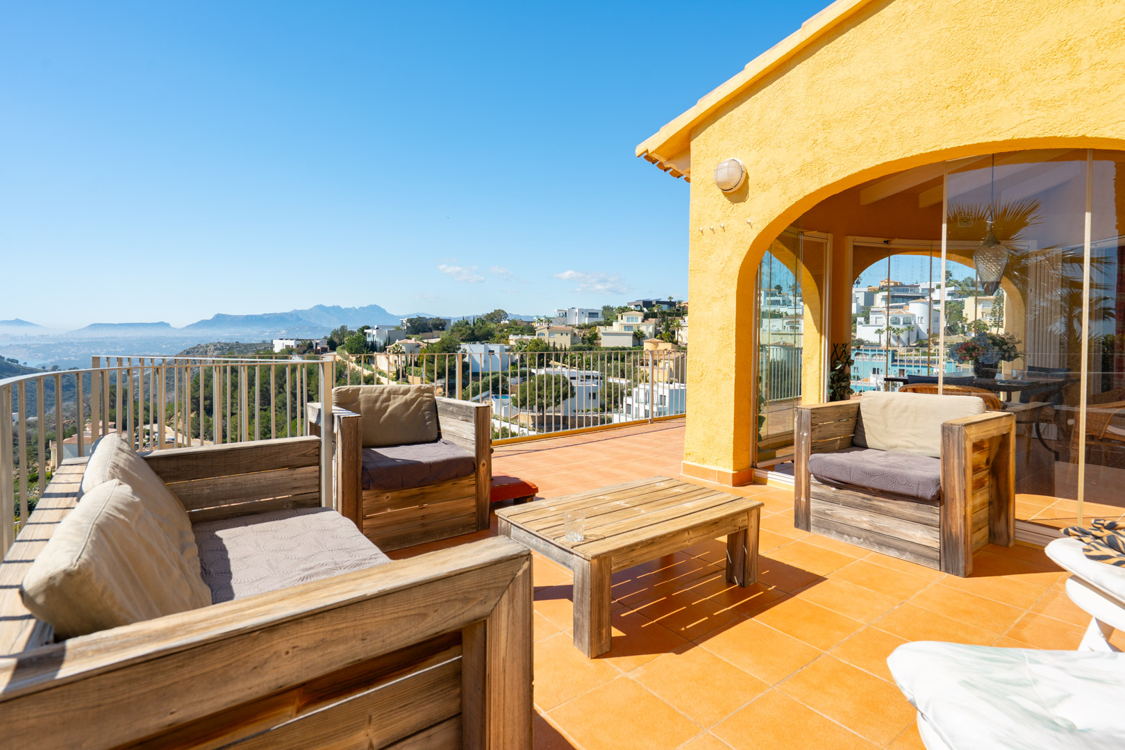 Solarium terrace featuring rustic wooden furniture, terracotta flooring, and panoramic views of the Mediterranean coast and Bernia mountains.
