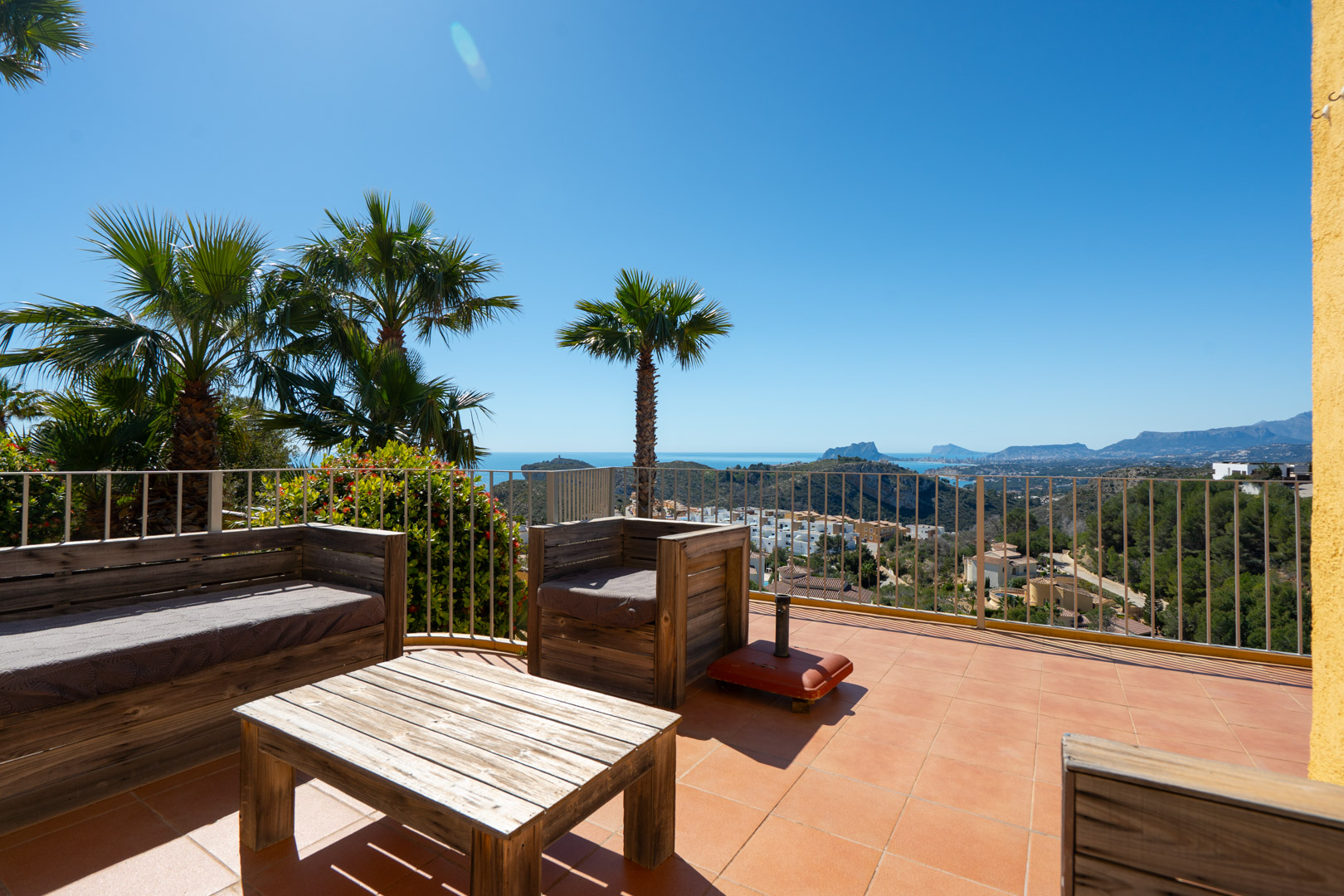 Solarium terrace featuring rustic wooden lounge furniture and panoramic views of the Mediterranean Sea, Peñón de Ifach, and the Calpe coastline.