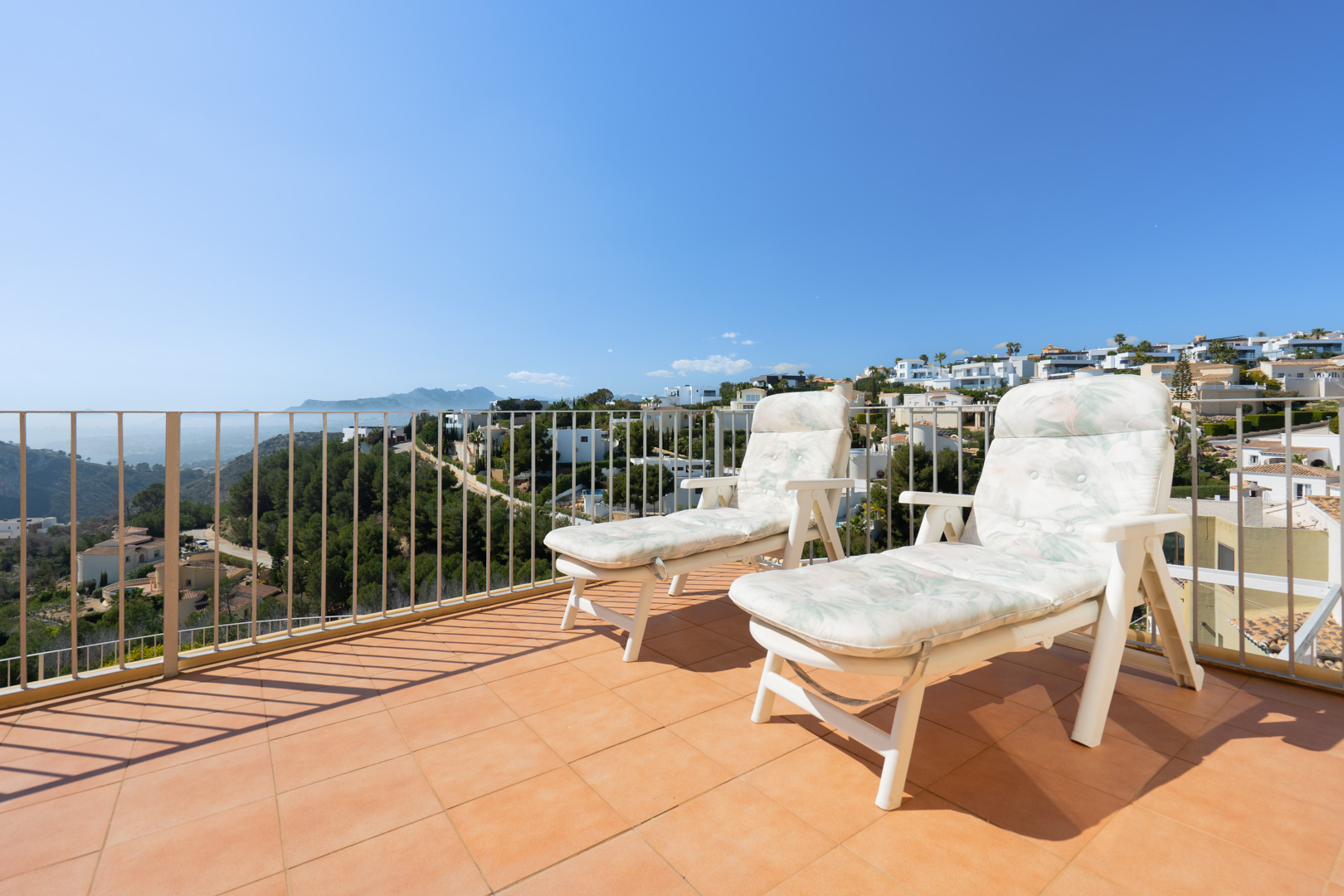 Solarium terrace featuring terracotta tiling and white railings, offering panoramic views of the Mediterranean coastline and the surrounding mountain ranges.