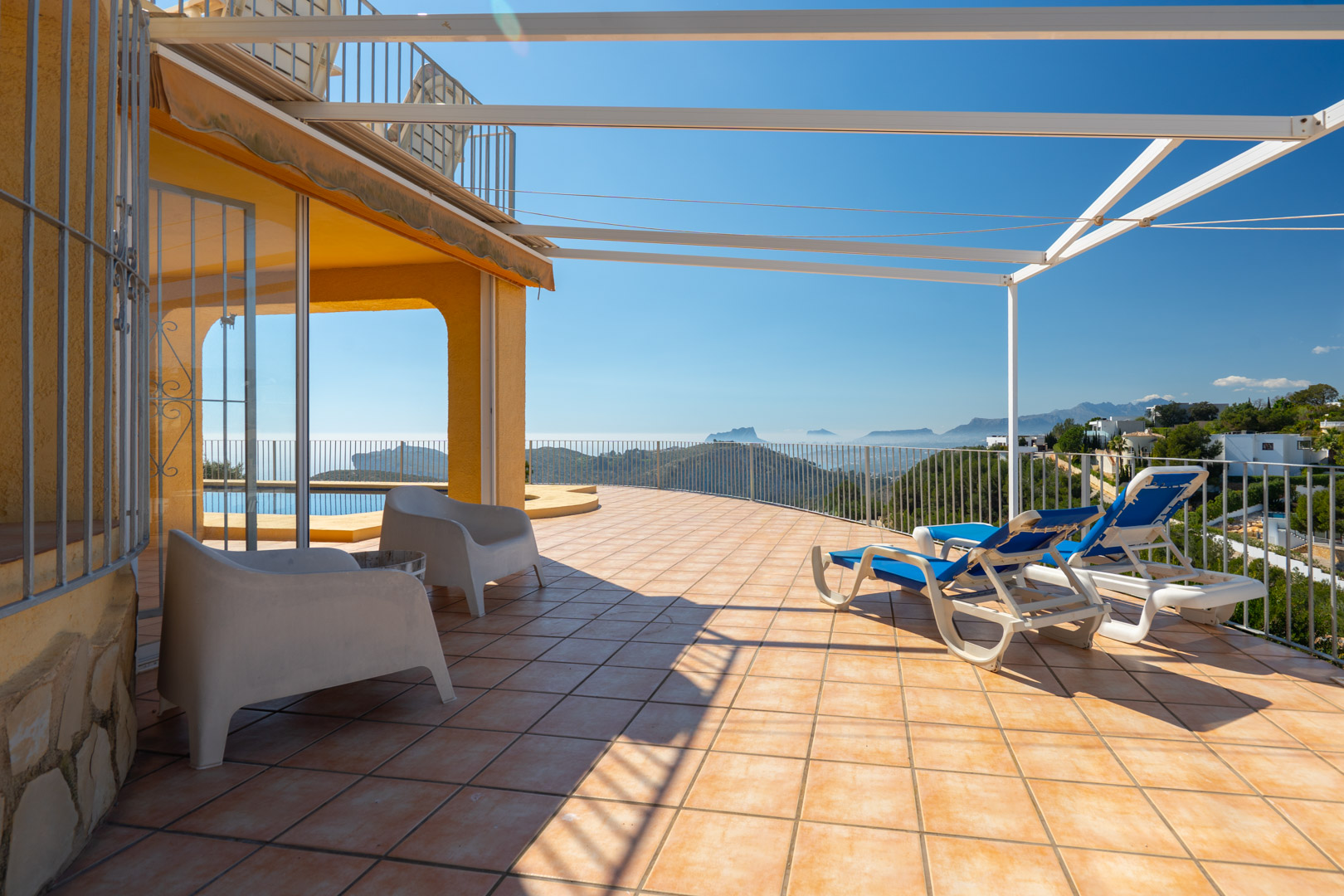 Spacious sun terrace featuring terracotta tiling, a metal pergola, and panoramic views of the Mediterranean coastline and Bernia mountains.