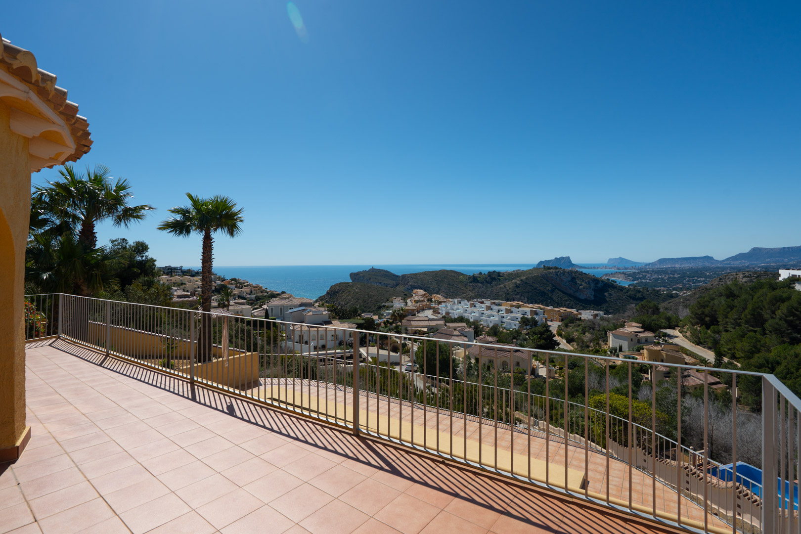 Spacious sun terrace with metal railings offering panoramic views of the Mediterranean coastline, the Peñón de Ifach, and surrounding mountains.