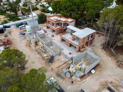 Aerial view of a residential complex under construction, featuring two villa structures with brick and concrete, multiple pool foundations, and a crane on site.