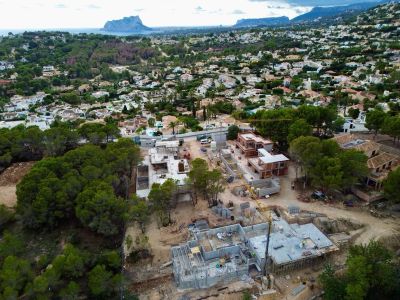 Aerial view of ongoing villa construction with concrete foundations and emerging brick structures, set within a lush green residential area, offering expansive sea and mountain views.