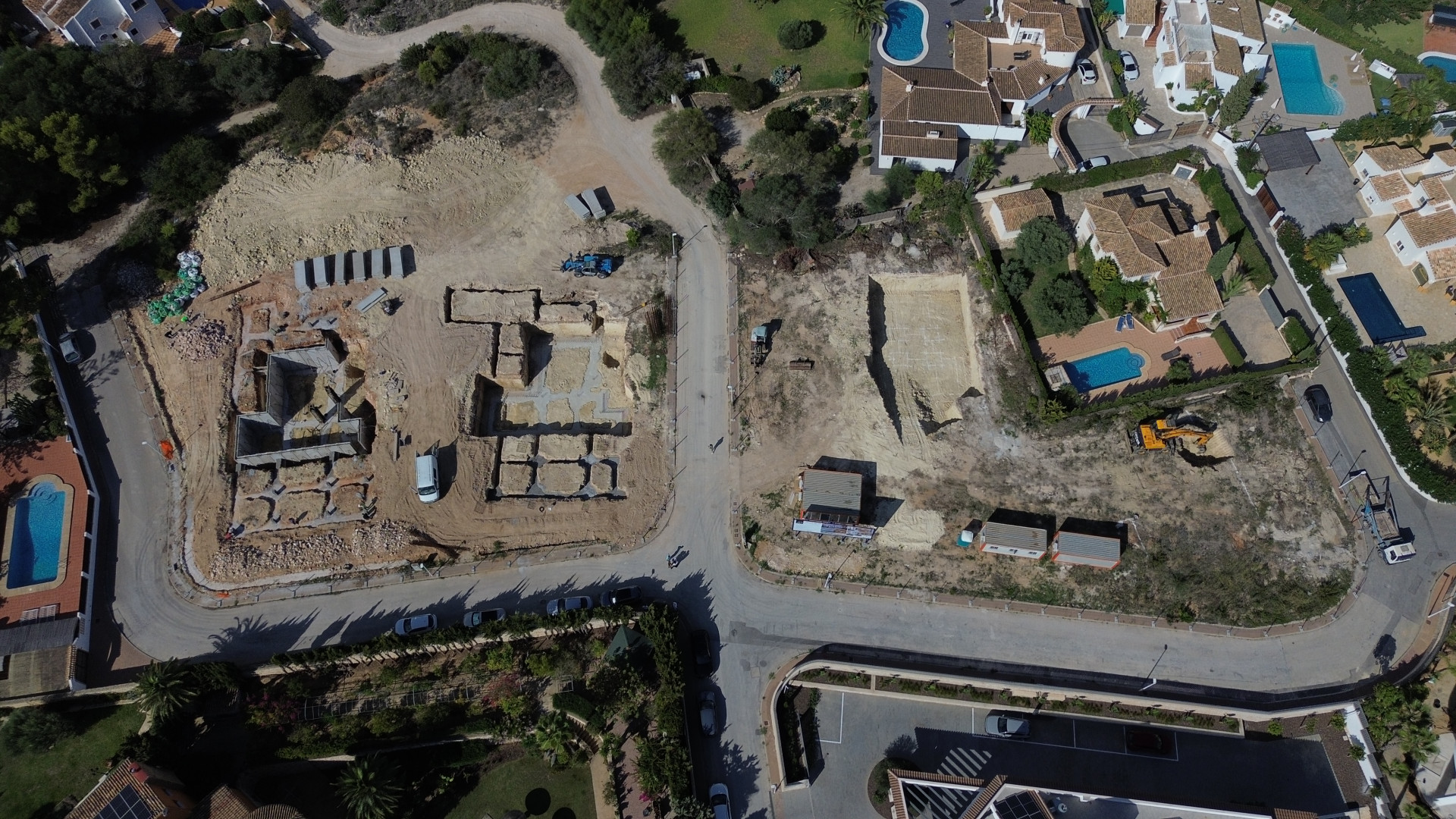 Aerial view of a residential development site in Jávea, showing concrete foundations laid for new villas and excavated plots alongside existing homes with private pools.