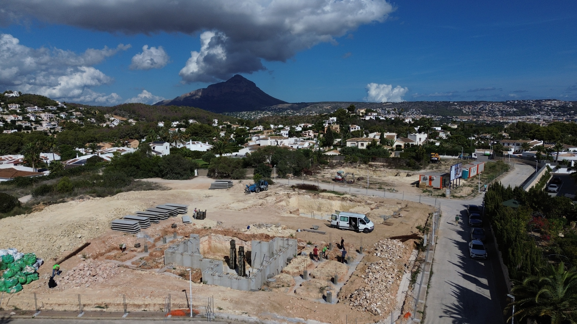 Aerial view of the Javea plot under construction, showing the villa's foundation and building materials. Residential homes and Montgó mountain are visible in the background.