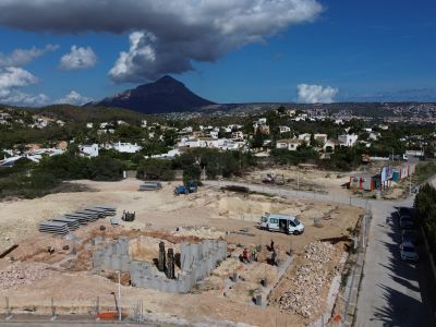 Aerial view of the Javea plot under construction, showing the villa's foundation and building materials. Residential homes and Montgó mountain are visible in the background.