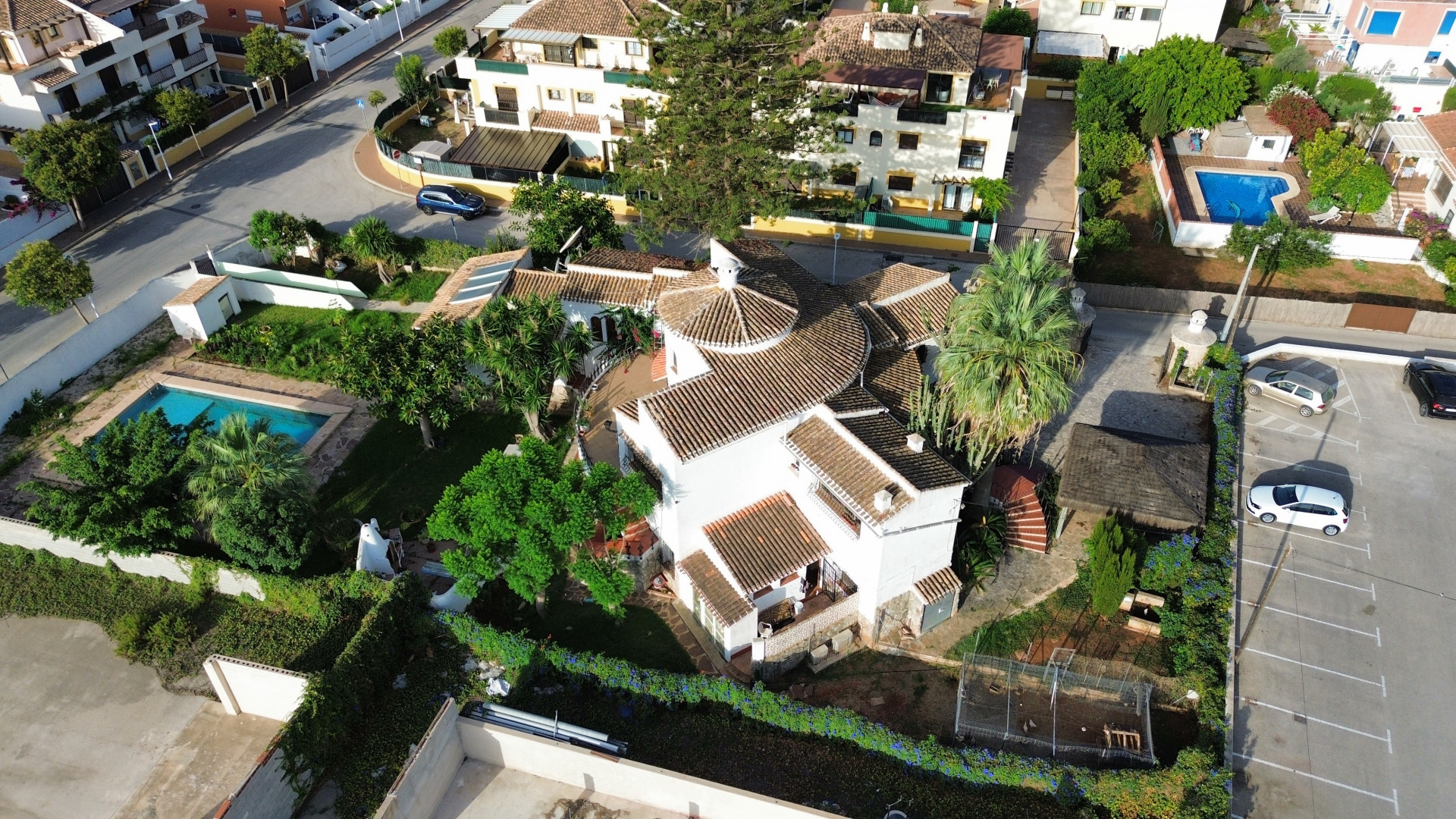 Aerial view of the villa with a tiled roof, a pool surrounded by greenery, and adjacent parking.